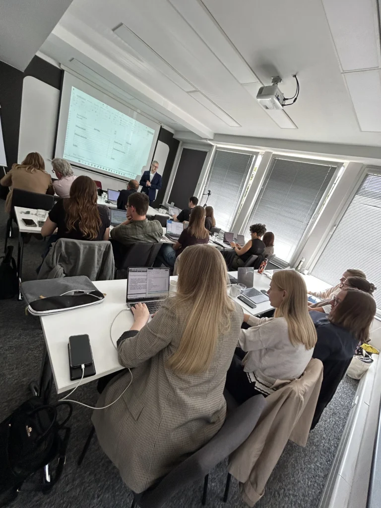 Zdjęcie ze szkolenia stacjonarnego: osoby z MATERIALITY pracują na laptopach, a prowadzący omawia materiały wyświetlane na ekranie.